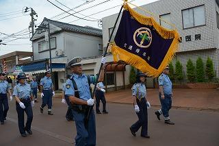 大きな旗を持った警察官が、他の警察官とともに道を練り歩いている写真