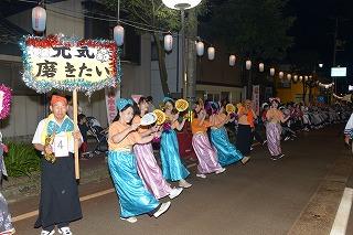 プラカードを持った人を先頭に横一列に並び、青やピンクの衣装を着て踊っている人たちの写真