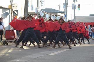 赤と黒の衣装を着た人たちが、両手と両足を大きく広げて立っている写真