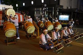 座って太鼓を叩いている人の列と、その後ろで立って太鼓を叩いている人たちの列を撮影した写真