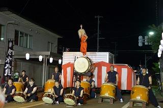 太鼓を演奏する人たちの後ろに、紅白幕のかかった台がある写真
