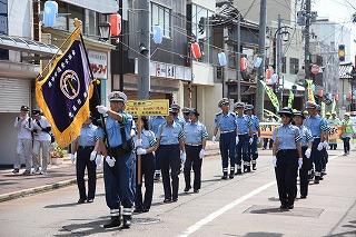 大きな旗を持った人を先頭に、青いシャツを着た警察官の人たちが行進している写真