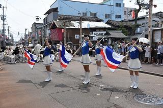 青と白の衣装を着た女性たちが、並んで旗を回している写真