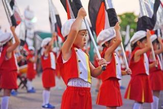 赤い衣装と白い帽子をかぶり、旗を持っている子供たちの写真