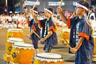 紺色のはっぴを着た男の子たちが、並んで和太鼓を叩いている写真