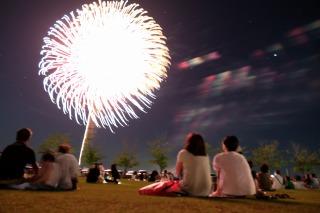 夜空に打ちあがった白い大きな花火と、座ってそれを見ている人たちの写真