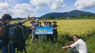 田んぼを背に、下町ロケットの看板を持ちながら撮影する人たちの写真