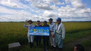 青空の下、看板を手に持ってカメラに向けて手を降る人の写真