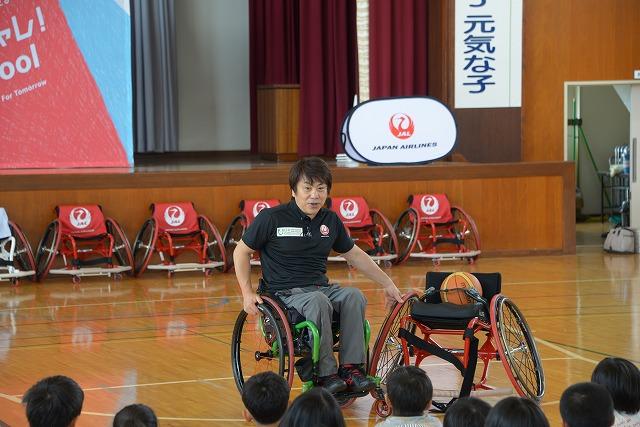 車椅子バスケットボール用の椅子を触りながら、話をしている車椅子に乗った男性の写真