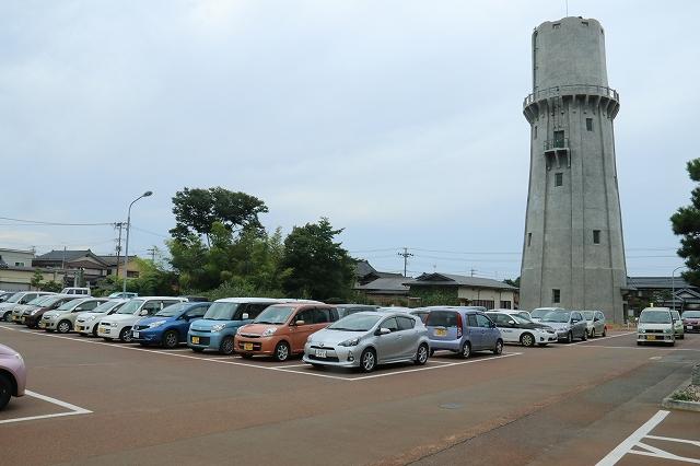 塔のような建物がある駐車場に、車がぎっしり並んでいる写真