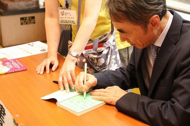 机の上で、年配の講師が本にサインをしている写真
