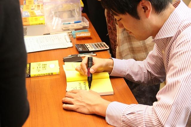机の上で、若い講師が本にサインをしている写真
