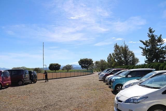 青い空のもと、車で埋まった駐車場の様子の写真