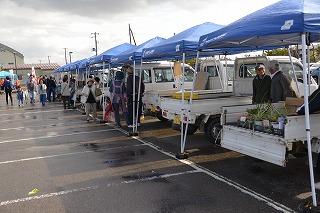 会場に並ぶ軽トラックとその荷台に積まれた野菜、軽トラックを覆うテントの様子