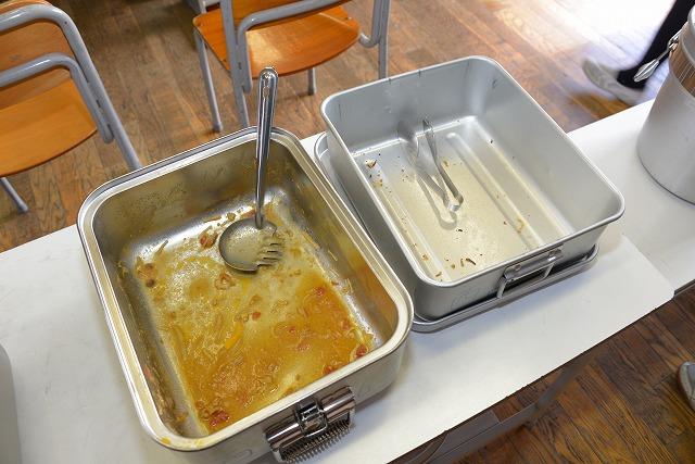 白い机に乗せられた料理をよそう道具が1つずつ入っている生徒たちに配り料理が空になった2つの金属製の大きな器の写真