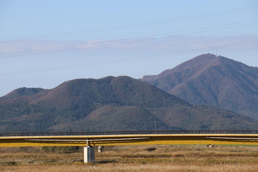 国上弥彦青空や山脈を背景に水のない川に建てられた黄緑色の横向きの橋の写真山