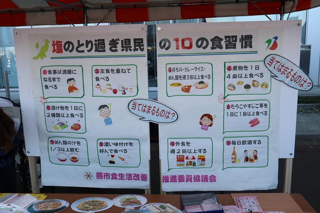 紅白のイベント用テントの中で吊り下げられている塩のとり過ぎ県民の10の食習慣と題する新潟県民の食習慣に関する10個の項目が書かれた2つの用紙の写真
