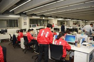 オフィス内で赤いジャンパーを着て仕事をしている人達の写真
