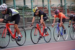 競技場内を走る生徒が乗った赤い3台の自転車と青い1台の自転車の写真