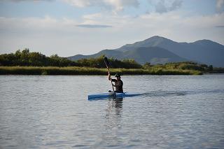 山脈と葉が茂った森林を背景に湖で青いボートを漕ぐ男子生徒の写真
