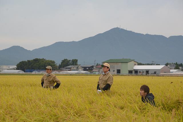 遠くに山脈が見える畑で三人の男性が立っている写真