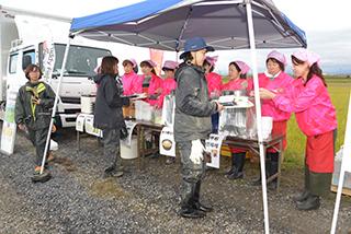ピンク色のジャンパーを着たスタッフが食事を配っている写真