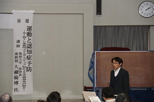 講演会で壇上に立って講演をする「スクエアステップ」開発者の大藏倫博氏の写真