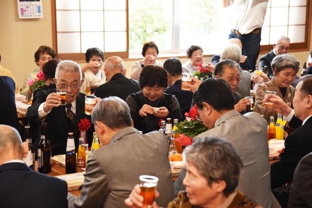 座ってビールやお酒で乾杯する熟年成人式参加者たちの写真