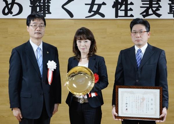 市長と並んで立つ盾を持つ女性と賞状を持つ眼鏡をかけた男性の写真
