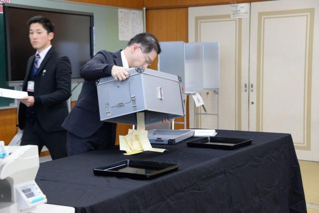 投票箱を開け投票用紙を机の上に出している市役所職員の写真