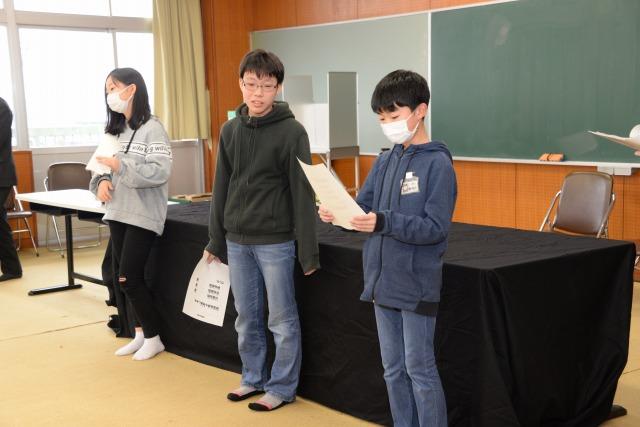 机の前で投票結果を発表する発表係の3人の小学生の写真