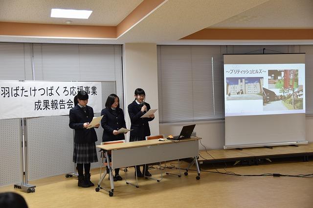 スクリーンの横で書類とマイクを手に、発表をしている制服姿の女生徒三人の写真