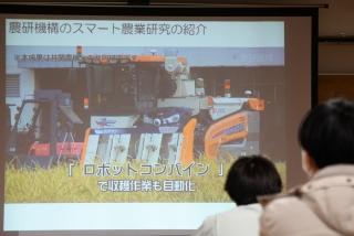 スクリーンに、農作業ロボットの映像が映し出されている様子と、それを見る参加者の写真
