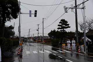 雨に濡れた車道の両脇に、縦型の信号機が立っている写真