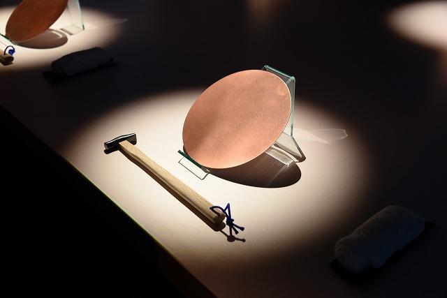 テーブルに置かれた円盤とトンカチが、スポットライトで照らされている写真