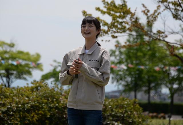 外で作業着を着てマイクを持っている女優の朝倉あきさんの写真