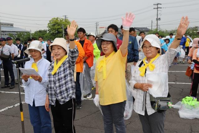 横に並んで手を挙げながら、宣誓をしている帽子を被った中高齢の女性グループ4人とそれを見守る人々の写真