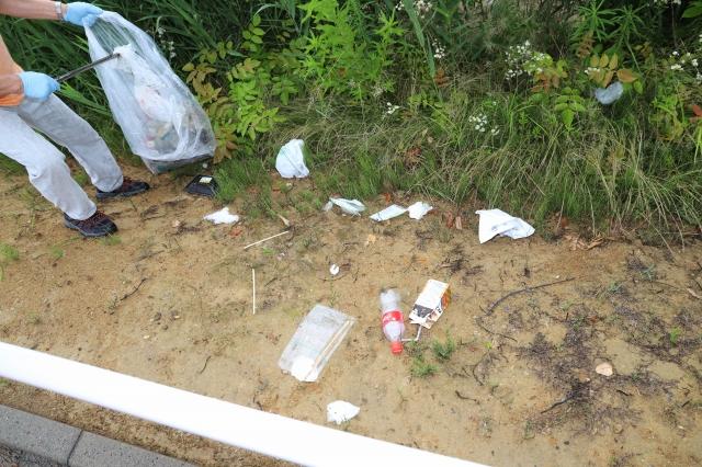 道路脇に散らばったペットボトルやビニール袋などのゴミを、トングで回収しゴミ袋に入れている参加者の写真