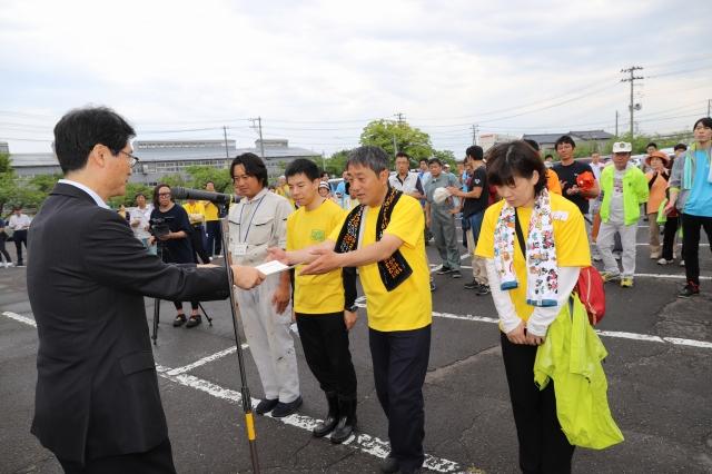 参加者達が見守る中、前に出て賞状を受け取る男女4人のグループと、賞状を手渡す黒いスーツ姿の男性の写真