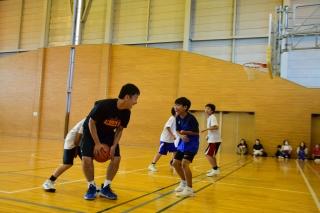 バスケットボールをキープしている男性と、それを阻止しようと動いている子ども達の写真