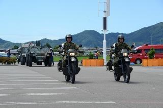 濃い緑色の制服を着た二人の人が、バイクで並走している写真