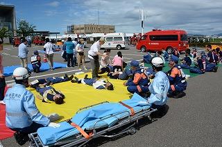 水色の服を着た隊員たちが、担架の横にしゃがみ、横になっている被災者役の人たちを見ている写真