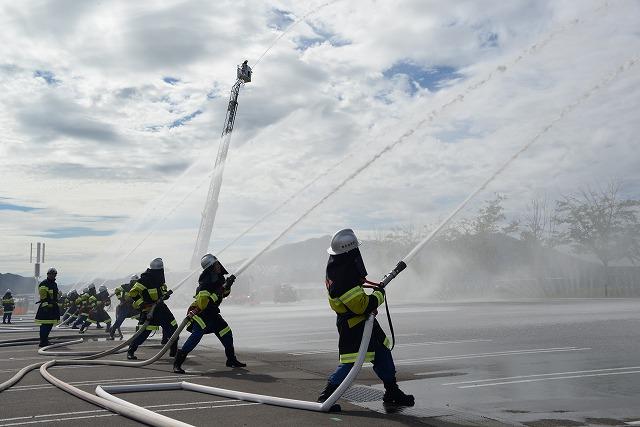 消防服の人たちが一列に並び、空に向かってホースで放水している写真