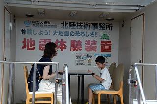 地震体験装置の中で、テーブルを挟んで向かい合って座る女性と男の子の写真
