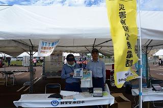 NTT東日本のブースに立ち、災害伝言ダイヤルの宣伝をしている二人のスタッフの写真