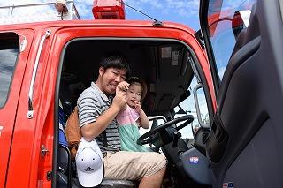 消防車に試乗しながらカメラに向かって手をふる親子の写真