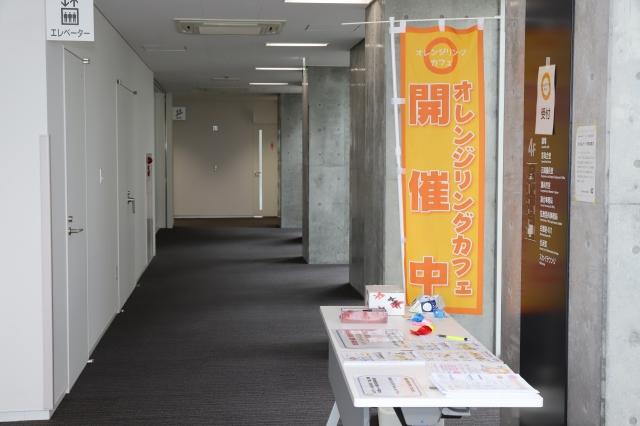 庁舎の廊下で、オレンジののぼりと資料の置かれた長机が並んでいる写真