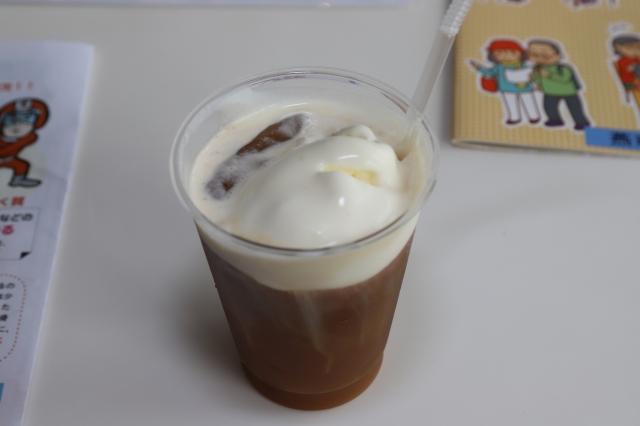 白いクリームが乗った茶色い飲み物が入った、透明なコップの写真