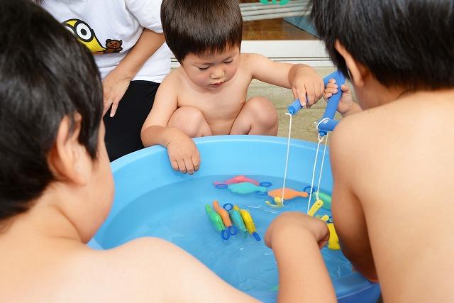 水が張られたたらいを囲み、釣りのゲームをしている男児たちの写真