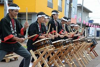 赤と黒のはっぴを着た人たちが、中腰になり、並んで和太鼓を叩いている写真